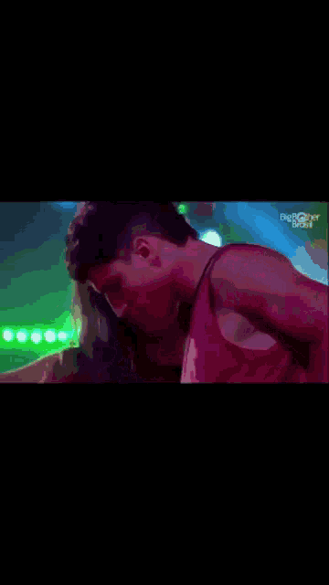 a man in a red tank top is kissing a woman in front of green lights