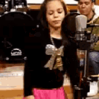 a little girl is singing into a microphone while a man looks on .