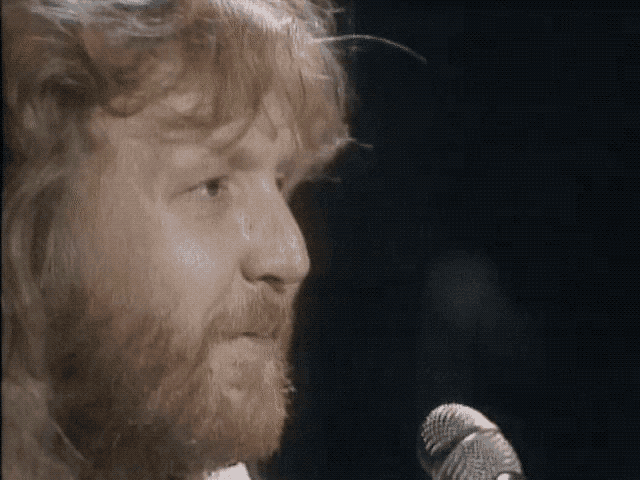 a man with a beard is singing into a microphone in a dark room