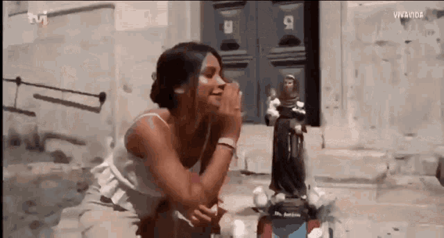 a woman is kneeling down in front of a statue with the tvi logo in the background