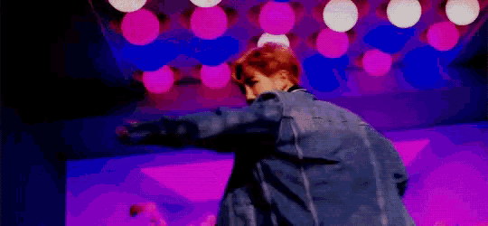 a man is dancing on a stage with his arms outstretched in front of a microphone .