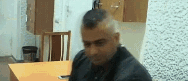 a man with a mohawk is sitting at a table with a phone in his hand .