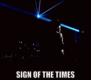 a group of people singing in front of a sign of the times logo
