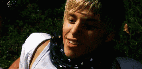 a young man wearing a scarf around his neck is laying in the grass and smiling .