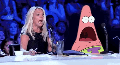 a woman sitting at a table with a microphone and patrick star behind her