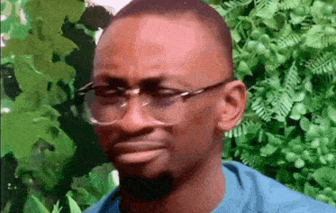 a man wearing glasses and a blue shirt is making a funny face in front of a green wall .