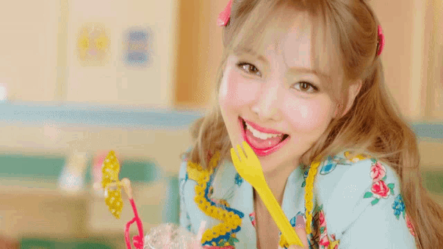a girl with blonde hair is holding a yellow fork in her mouth and smiling