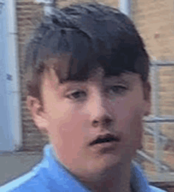 a young boy in a blue shirt is standing in front of a brick building and making a funny face .