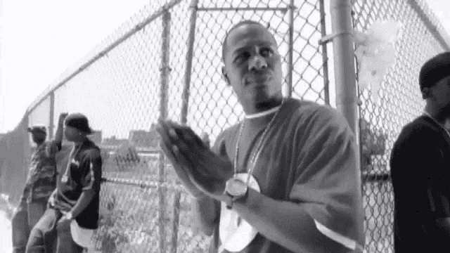 a man is standing in front of a chain link fence with his hands folded .