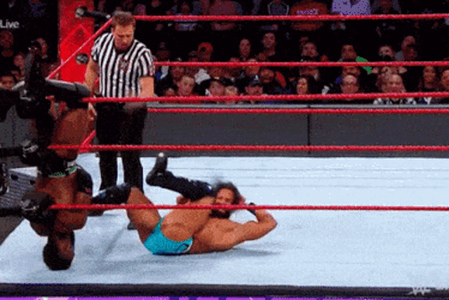 two men are wrestling in a wrestling ring with a referee in the background
