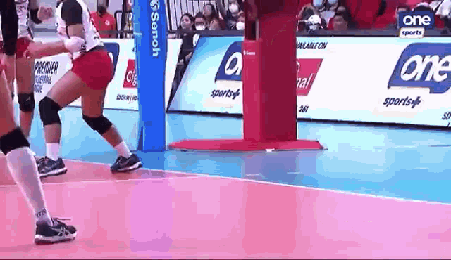 a woman is playing volleyball on a court with advertisements for one sports on the sidelines .