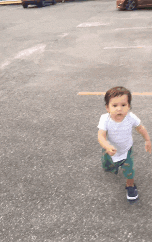 a toddler wearing a white shirt and green shorts is walking on a road