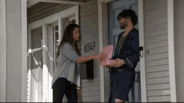 a man and a woman are standing in front of a house with the number 6547 on the front door