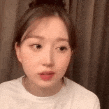 a close up of a woman 's face wearing a white shirt and a bun .