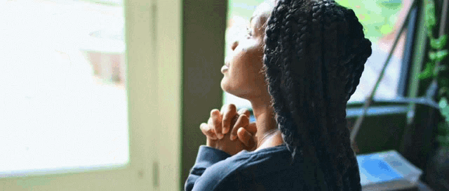 a woman is praying in front of a window with her hands folded in prayer .