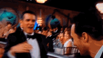 a man in a tuxedo is talking to another man in a crowd at a party .