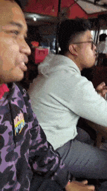 two men are sitting at a table in front of a sign that says ' bakso ' on it