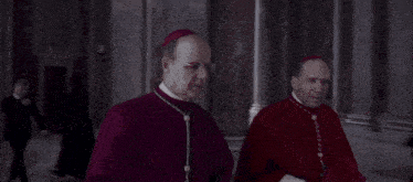 two priests in red robes are standing in a dark room