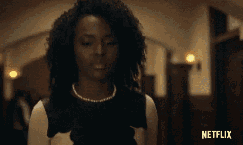 a woman with curly hair is standing in a hallway with her eyes closed .