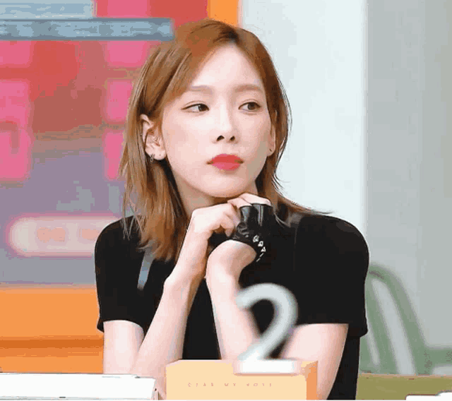 a woman wearing a black shirt and gloves is sitting at a table with her hands folded .