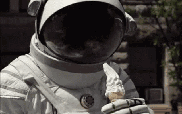an astronaut is eating an ice cream cone while wearing a helmet .
