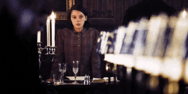 a girl is sitting at a table with candles and glasses .