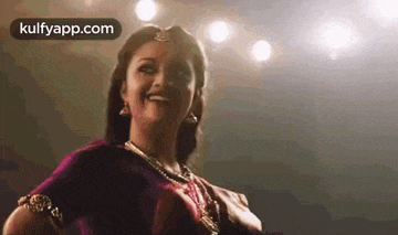a woman in a purple saree is smiling in front of a crowd .