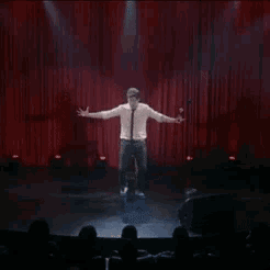 a man stands on a stage with his arms outstretched in front of a crowd