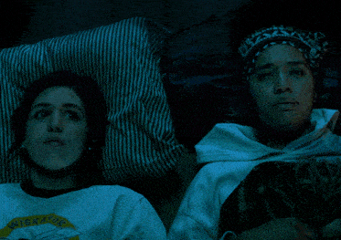 two women are laying on a bed and one has a shirt that says niskatuk