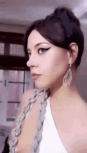 a woman wearing a white dress and earrings is standing in front of a window .