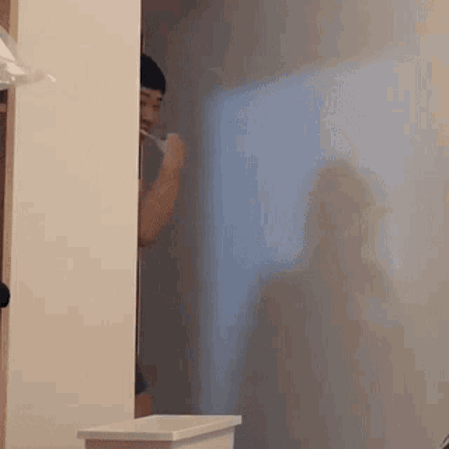 a man is brushing his teeth in a bathroom while peeking through a doorway .