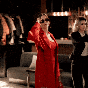 a woman in a red coat and sunglasses stands next to another woman in a suit