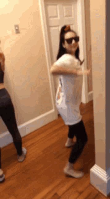 a woman wearing sunglasses is dancing in a hallway with another woman