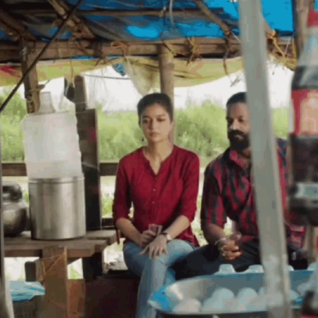 a man and a woman are sitting at a table in a hut .