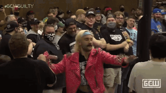a man in a pink jacket stands in front of a crowd with the hashtag #gcwguilty