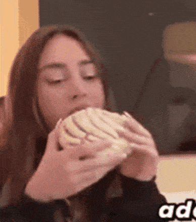 a woman is eating a sandwich with her hands while sitting at a table .