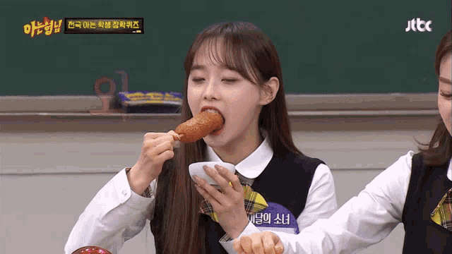 a girl in a school uniform is eating a chicken leg with a jtbc logo in the background