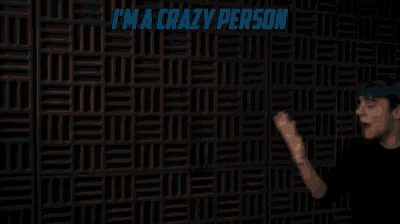 a man with blue hair is standing in front of a wall with the words i 'm a crazy person written on it