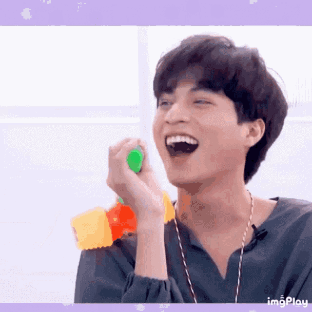 a young man is laughing while holding a green toy in his hand .