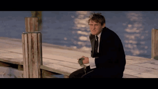 a man in a suit and tie is sitting on a wooden dock