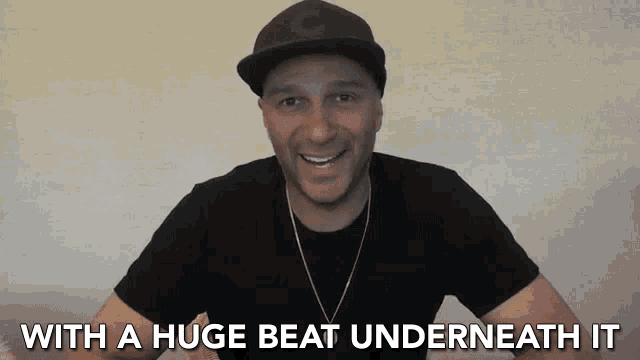 a man wearing a hat and a black shirt says " with a huge beat underneath it " in white letters