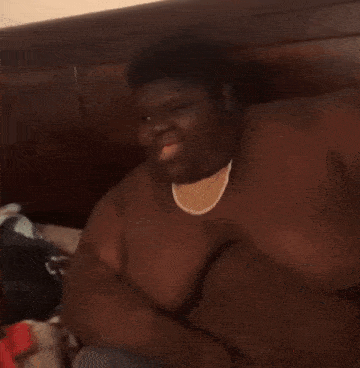 a very fat man is sitting on a bed wearing a watch and smiling .