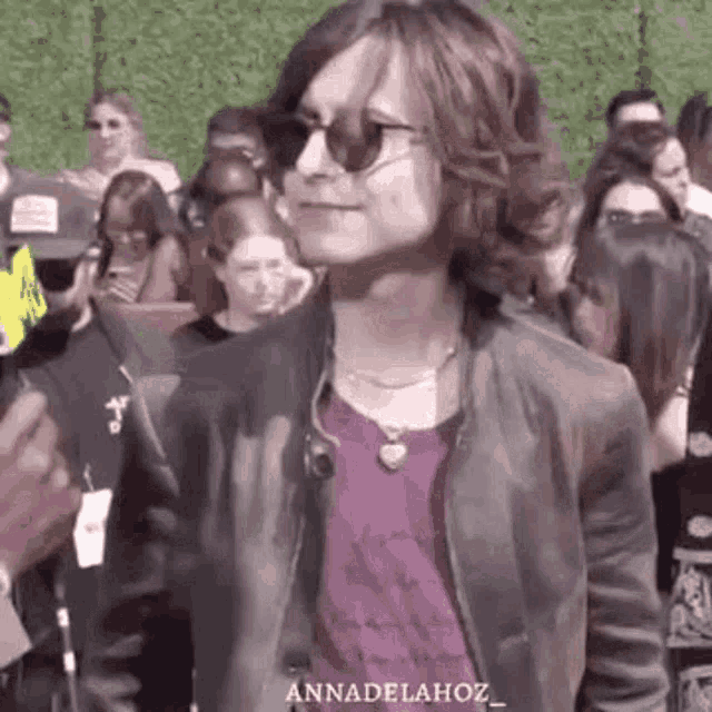 a man wearing sunglasses and a purple shirt is standing in front of a crowd .