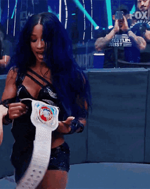 a woman with blue hair is holding a championship belt in front of a crowd .