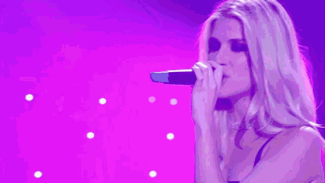 a woman is singing into a microphone on a purple background