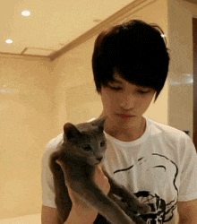 a man in a white shirt is holding a small grey cat