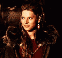 a woman wearing a fur coat and earrings smiles for the camera