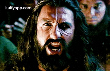 a man with a beard and long hair is screaming in front of a crowd of people .