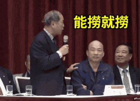 a man in a suit holds a microphone in front of two other men with chinese writing behind them