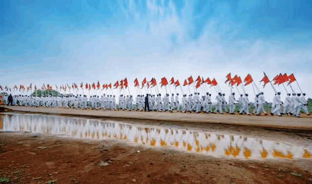 a large group of people marching down a dirt road with red flags